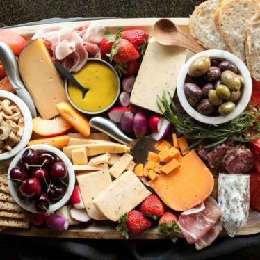 Cheese board with mangos, olives, and cherries